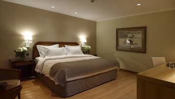 Habitación de hotel con una cama grande, mesitas de noche con lámparas, un escritorio y un cuadro en la pared.