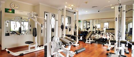 A gym with exercise machines, mirrors, and a clock on the wall.