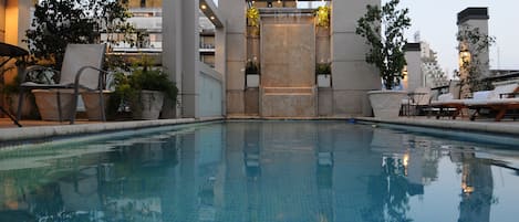 A swimming pool with a modern architectural design, surrounded by lounge chairs and potted plants.