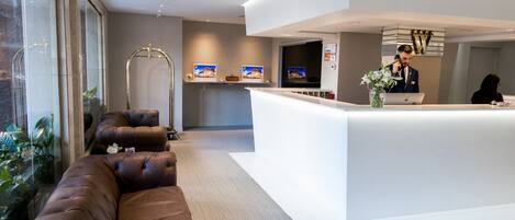 A modern reception area with a white counter, leather sofas, and a large window with plants.