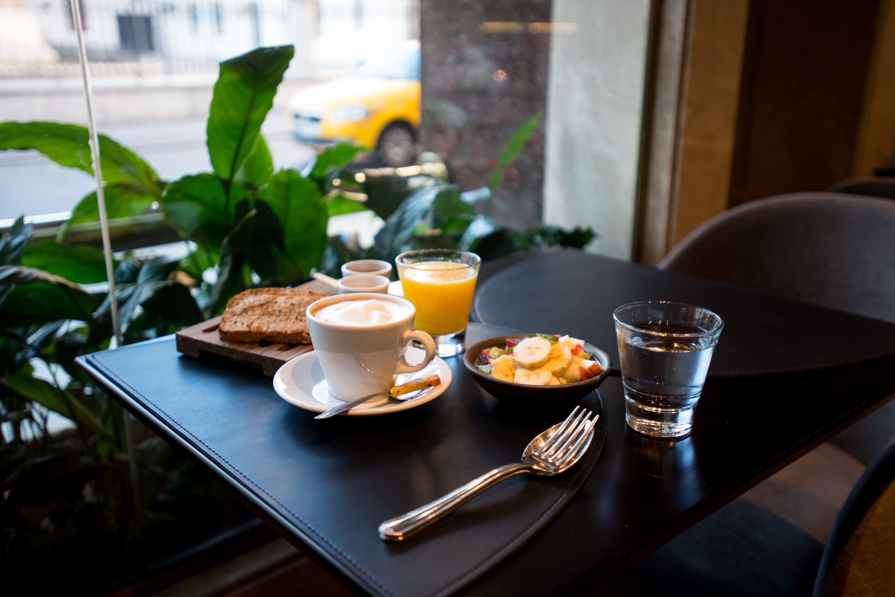 A breakfast table with toast, a cup of coffee, a bowl of fruit, a glass of orange juice, and a glass of water.
