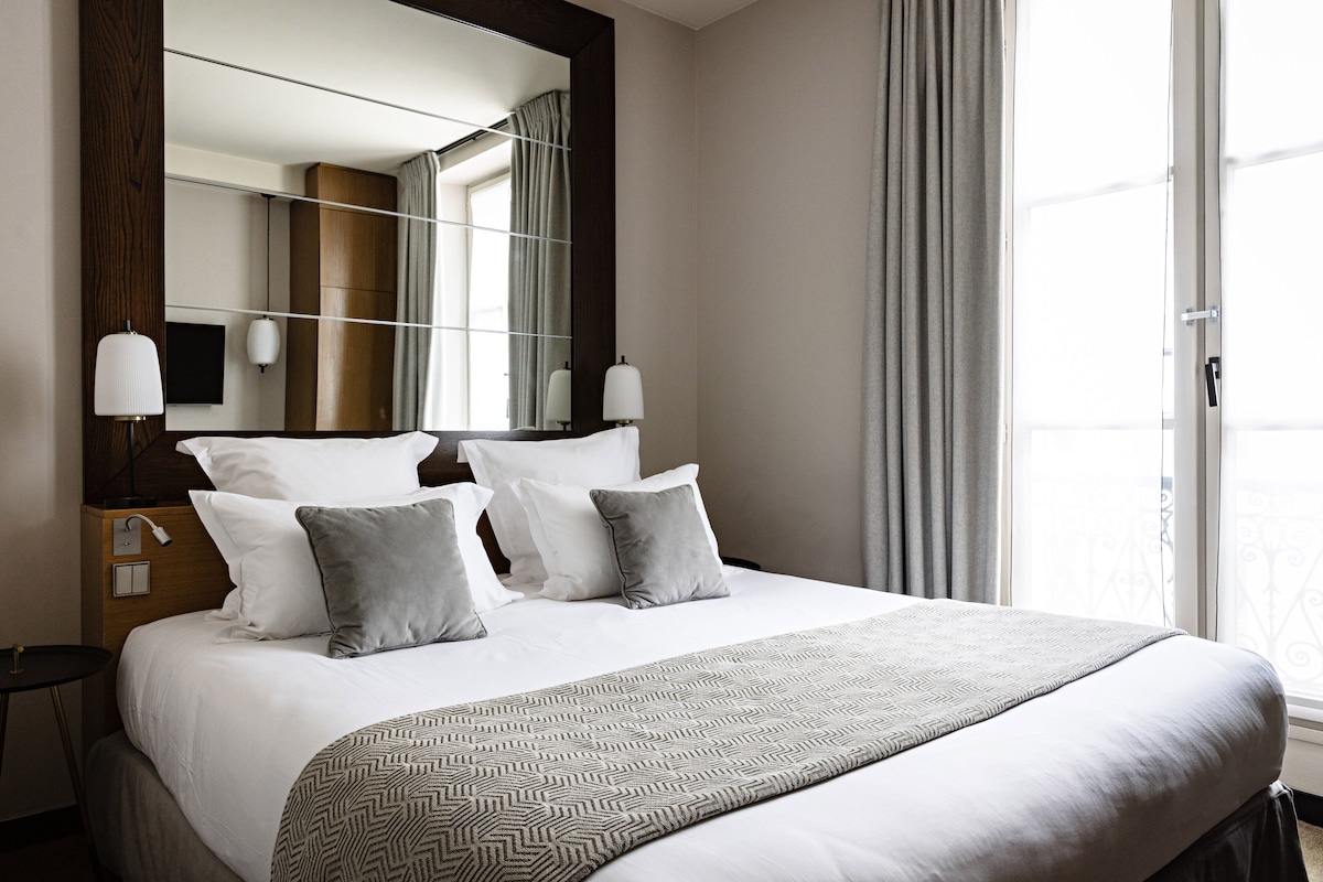 A neatly made bed with a patterned throw, a large mirror, and a bedside table with lamps.