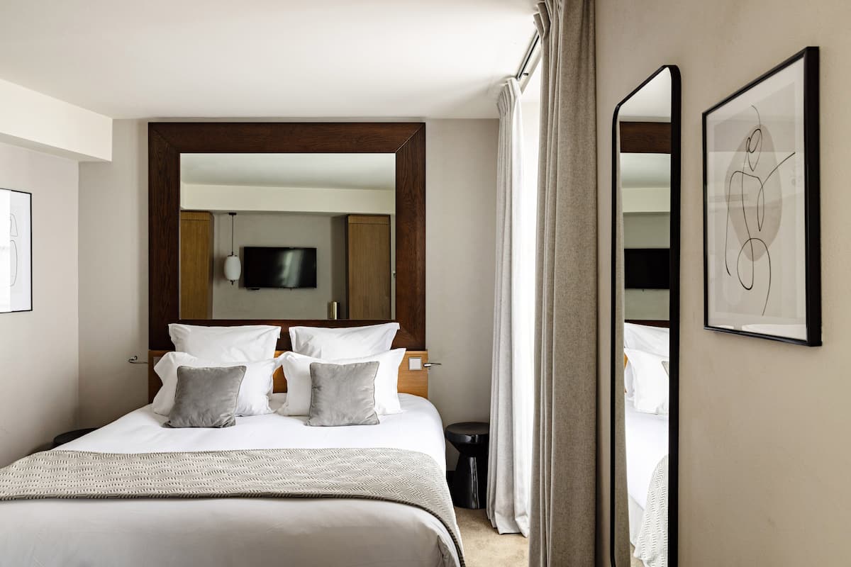 Une chambre d’hôtel bien aménagée, avec un grand lit, une table de chevet, un téléviseur à écran plat et une œuvre d’art abstraite encadrée accrochée au mur.