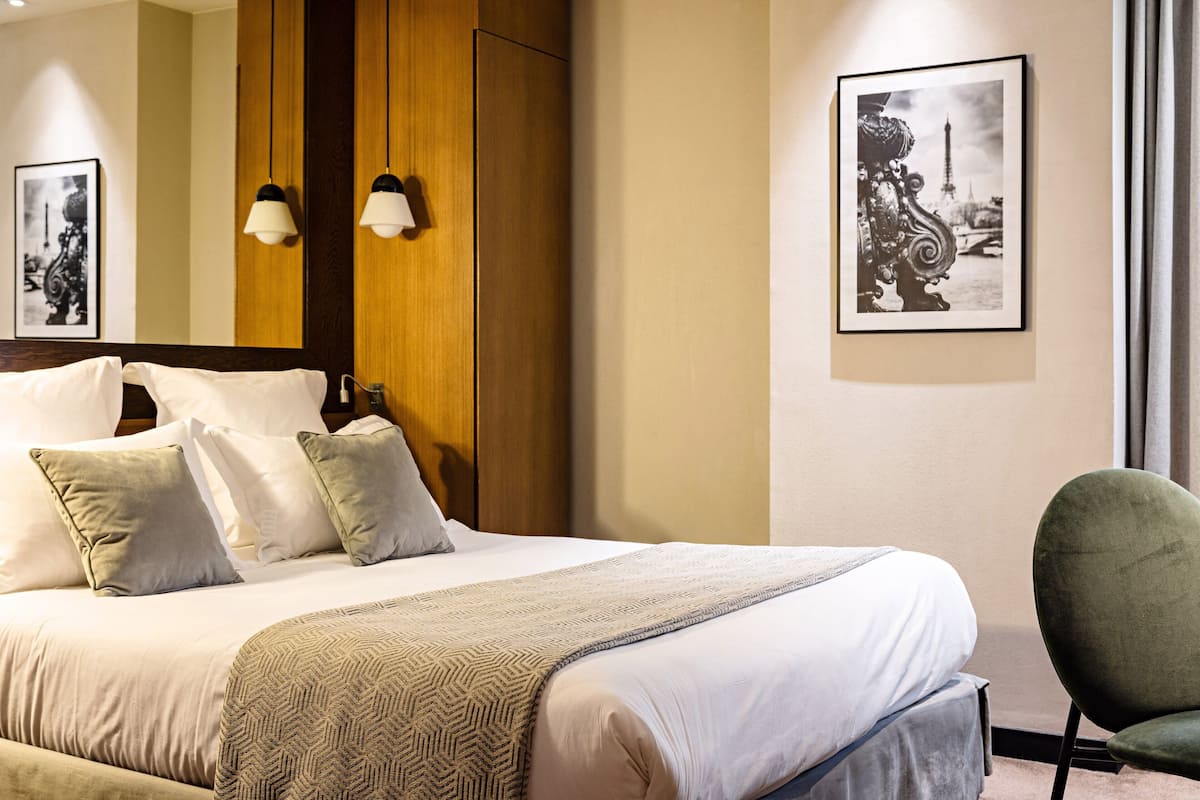 Un lit bien fait, agrémenté d’un couvre-lit à motifs, d’une tête de lit en bois et de deux lampes fixées au mur.