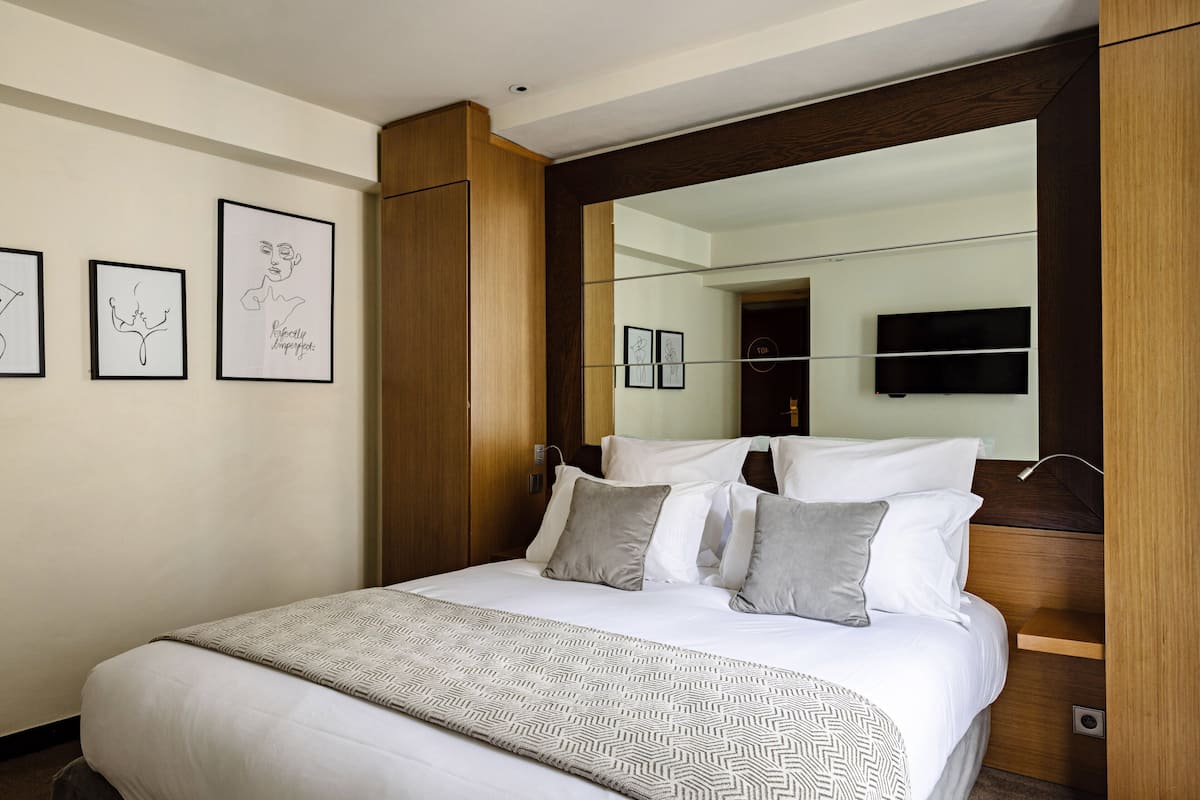 Une chambre d’hôtel moderne avec un grand lit, une tête de lit en bois, un téléviseur à écran plat et des œuvres d’art encadrées accrochées au mur.