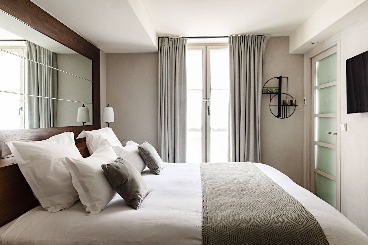 Habitación de hotel moderna con una cama grande, un espejo, un reloj en la pared y vistas por la ventana.