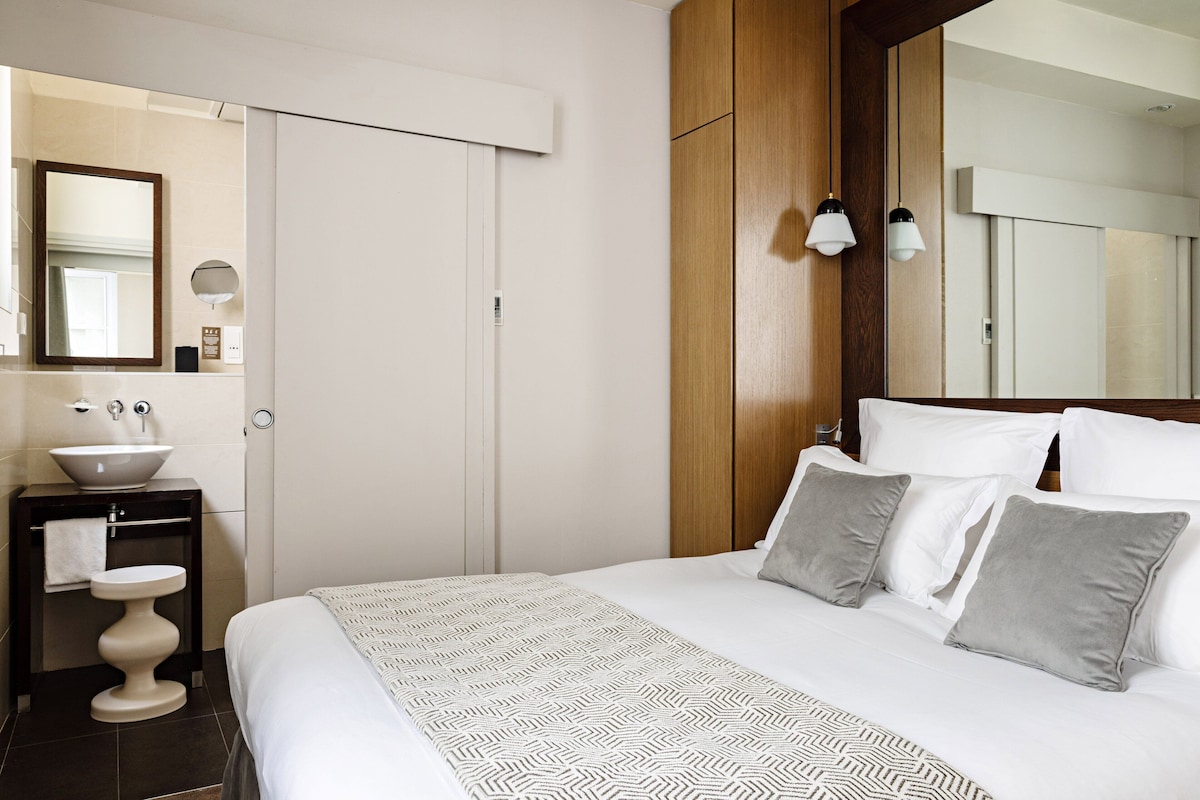 Una habitación de hotel con cama, mesita de noche con lavamanos, espejo y armario.