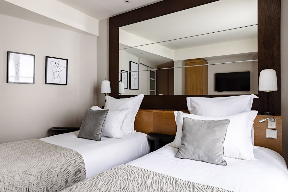 Une chambre d’hôtel avec deux lits, un grand miroir, une télévision et des œuvres d’art accrochées au mur.