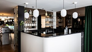 Zona de bar moderna con mostrador de mármol, lámparas colgantes y estantes llenos de copas y botellas.