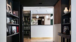 Un interior moderno con un espacio central abierto que conduce a un bar, rodeado de estanterías con diversos objetos y un suelo estampado.
