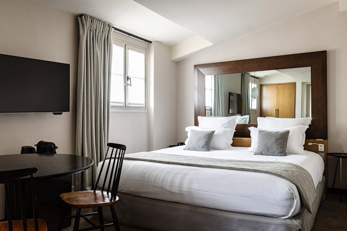 A hotel room with a bed, a TV, a dining table, and a chair.