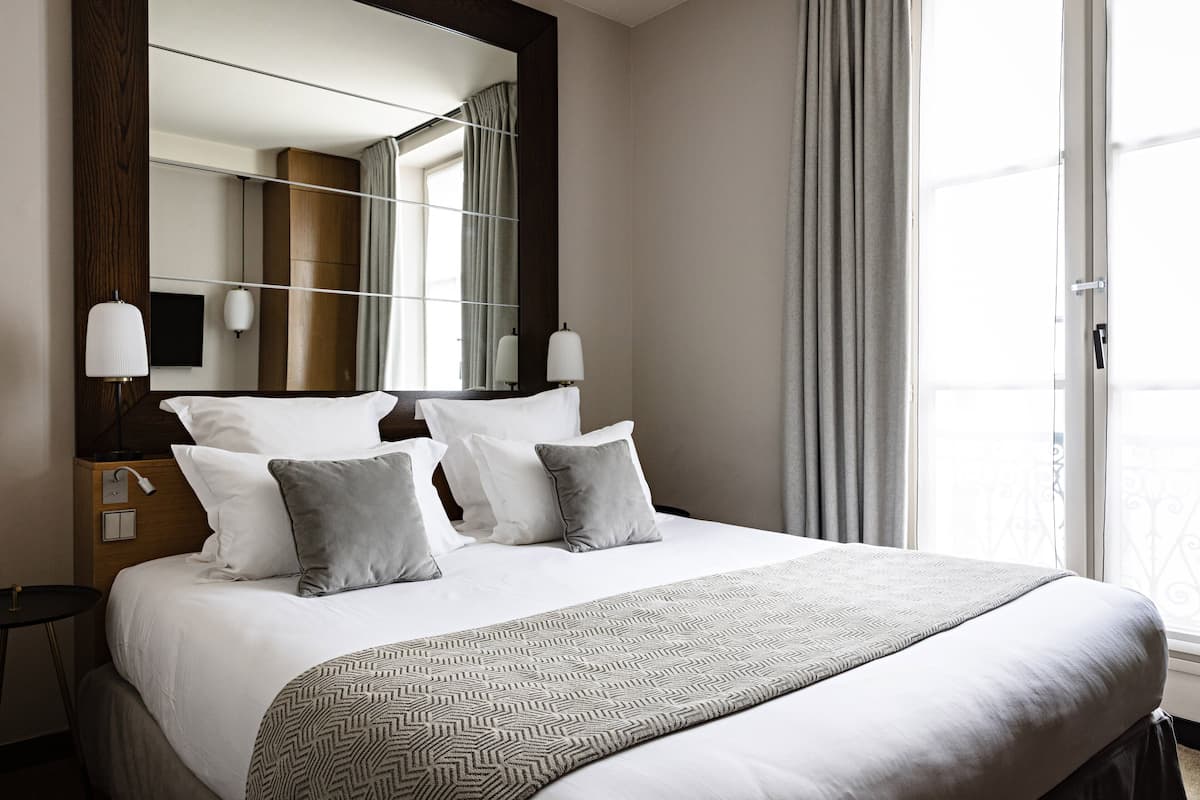Un lit bien fait, agrémenté d’un couvre-lit à motifs, un grand miroir et une table de chevet avec des lampes.