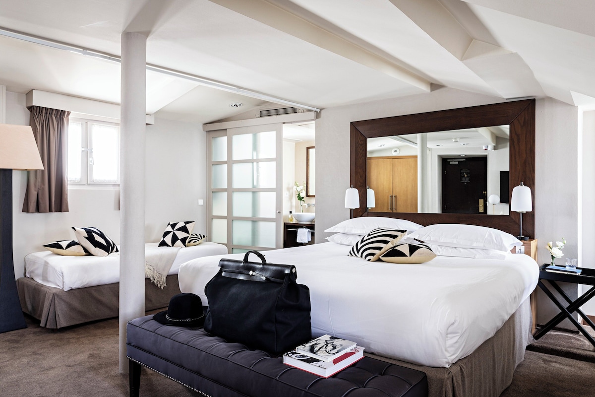 A hotel room with a large bed, a bedside table, a chair, a desk, and a mirror.