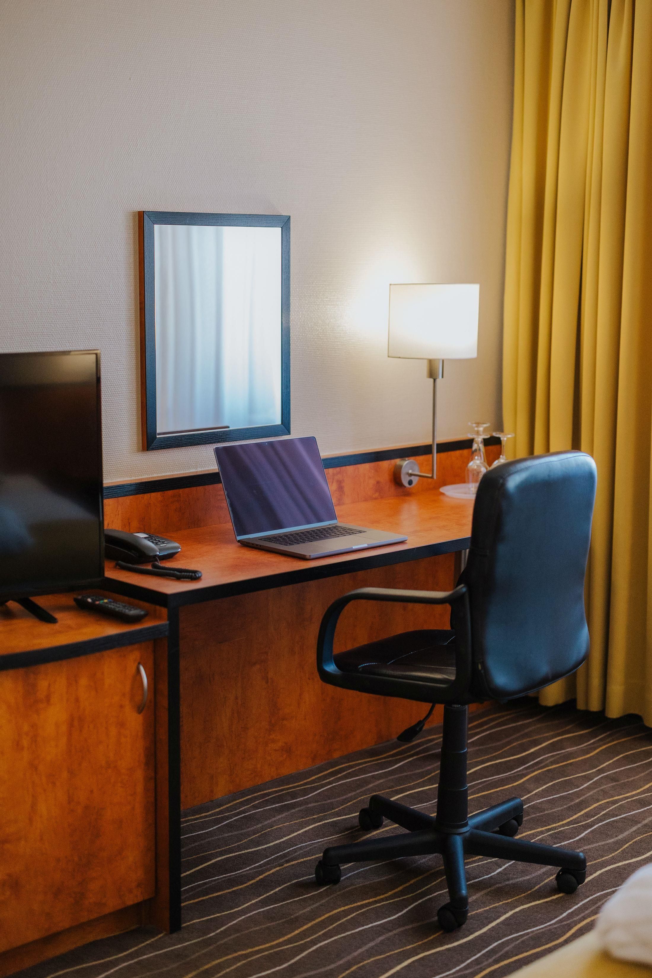 Habitación de hotel con escritorio, laptop, silla, televisor y lámpara.