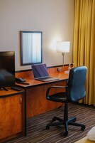 Habitación de hotel con escritorio, laptop, silla, televisor y lámpara.