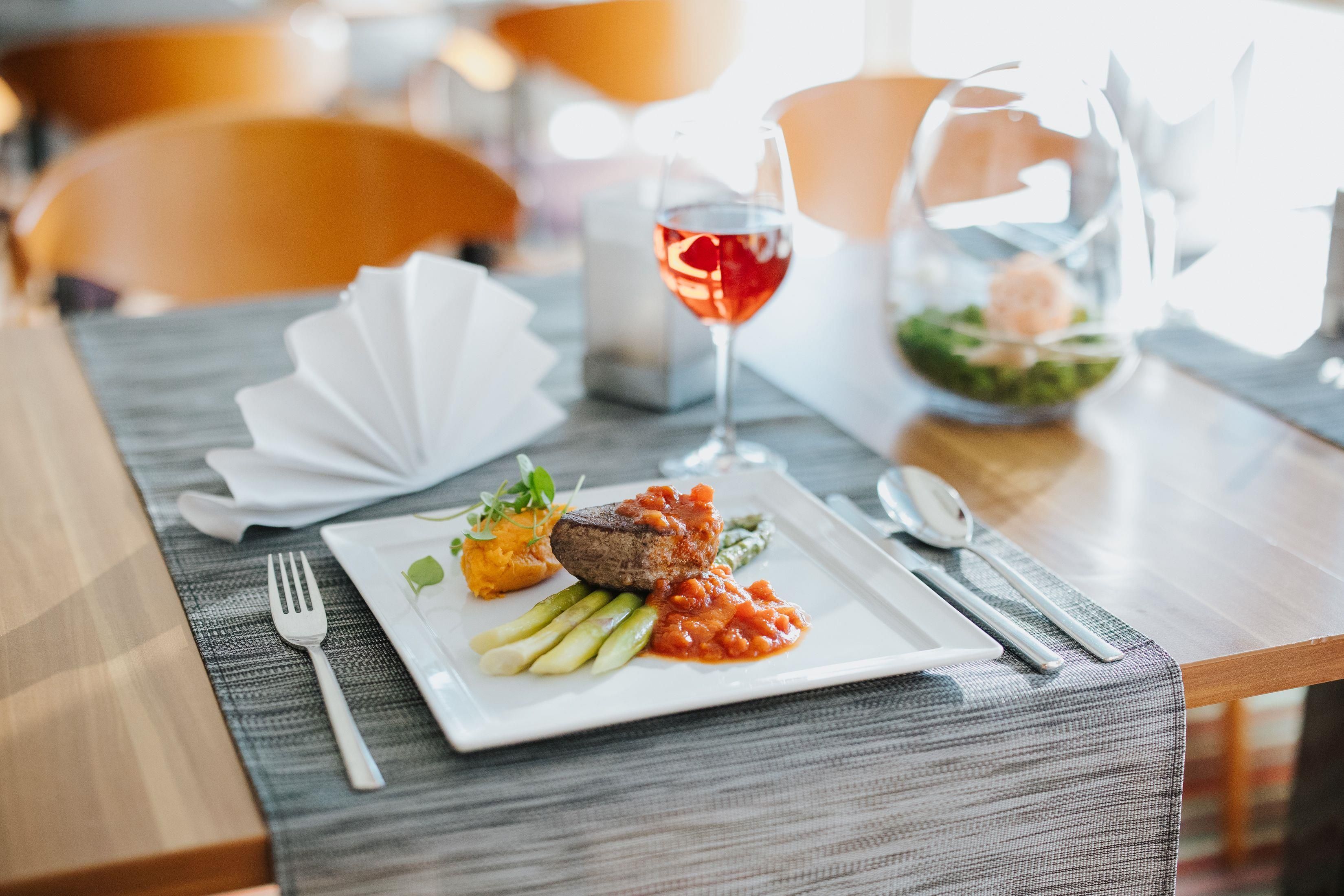 A dining table with a plate of food, a fork, a glass of red wine, and a bowl of salad.