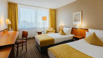 A hotel room with two beds, a desk, a chair, a small table, and a window with curtains.