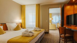 Habitación de hotel con cama, escritorio, silla, televisión y baño visible a través de una puerta abierta.