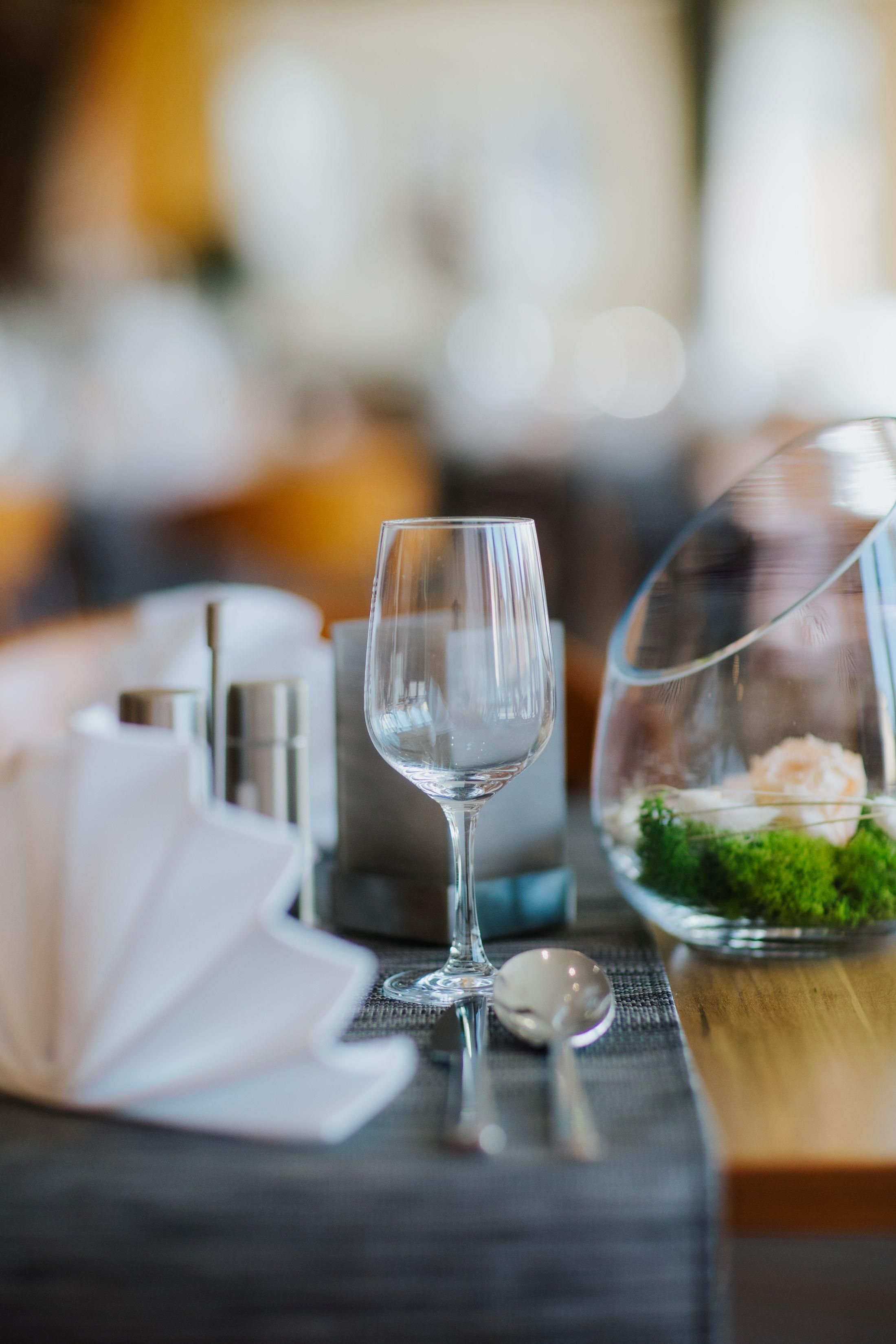 Une table à manger avec un verre à vin en verre transparent, un petit bol contenant une fleur et une cuillère.