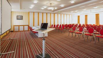 A conference room with a carpeted floor, a table with a laptop, and rows of red chairs.