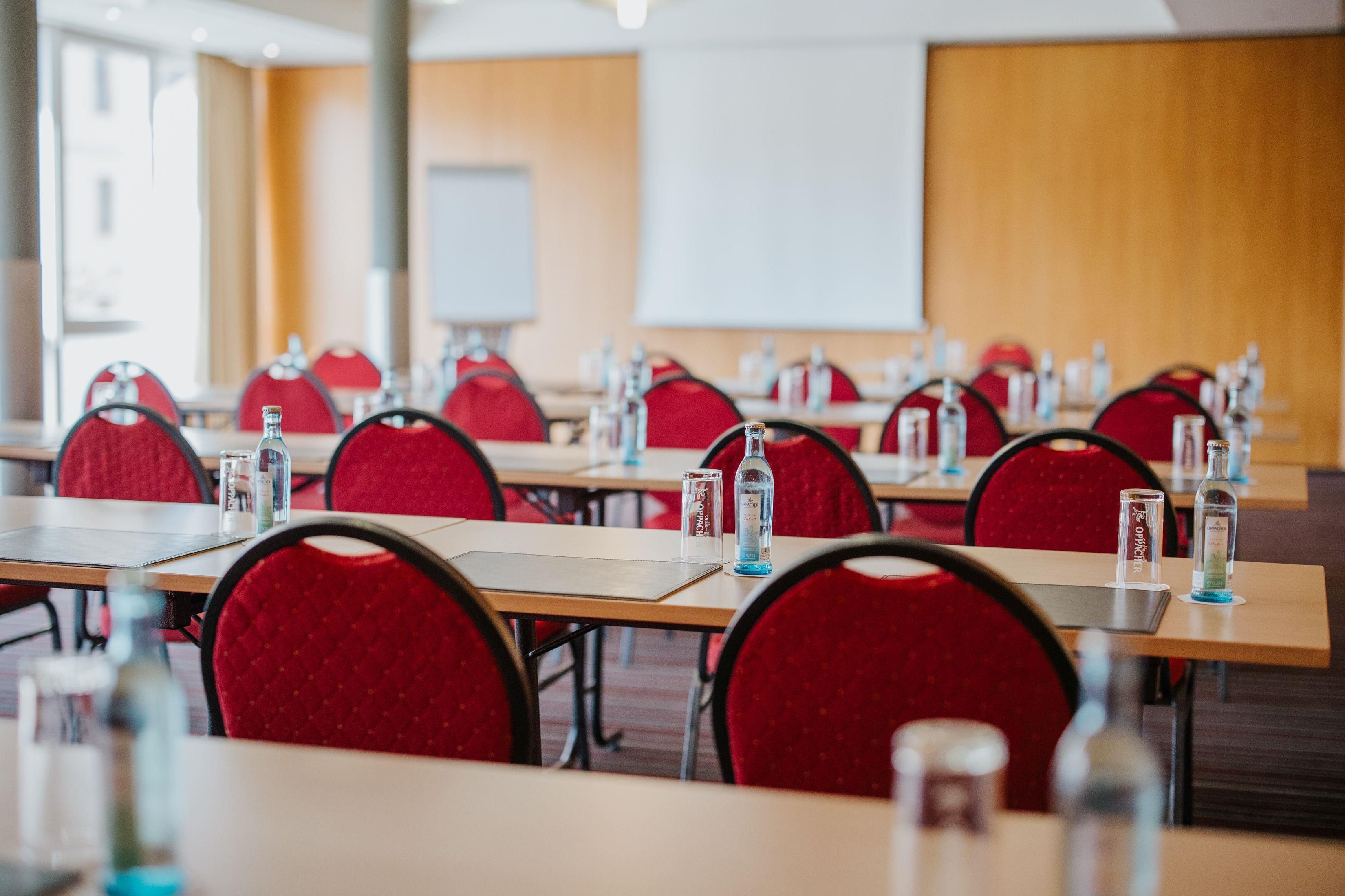 A conference room with rows of tables, red chairs, and water bottles.