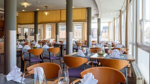 Un restaurante con mesas dispuestas para comer, amplias ventanas y vistas a la ciudad.