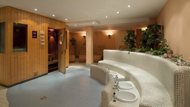 A spa area with wooden walls, a massage chair, a reception desk, and a seating area with a patterned sofa. - Best Western Plus Hotel Bautzen (Bautzen)