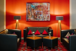 Un espace salon moderne avec un mur rouge, un canapé en cuir noir, deux fauteuils, une table basse et deux lampadaires.