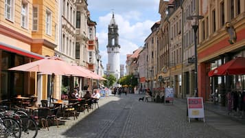 A cobblestone street lined with historic buildings, outdoor seating, and a clock tower in the distance.