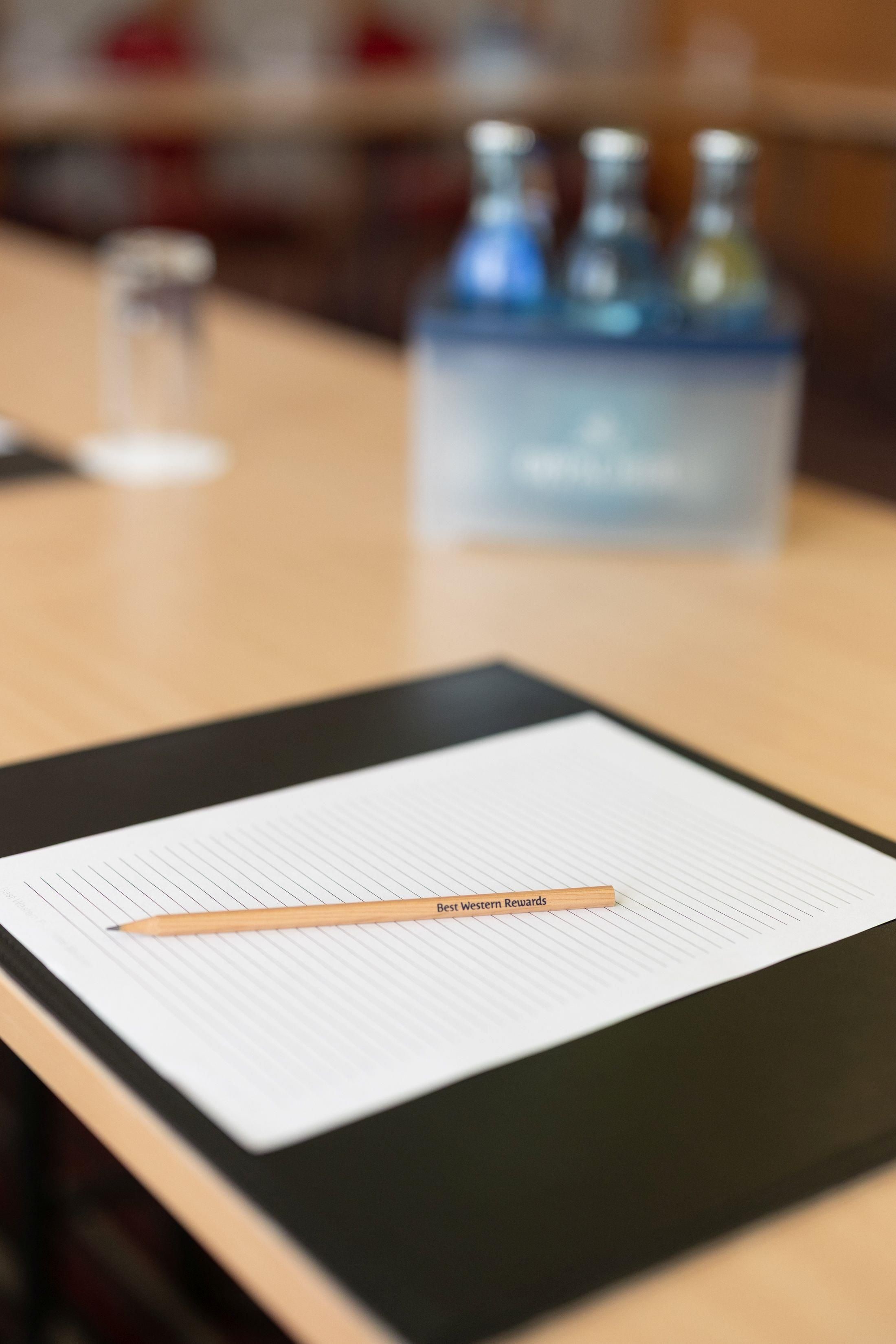 A clipboard with lined paper and a pencil, a water bottle, and a glass on a table.