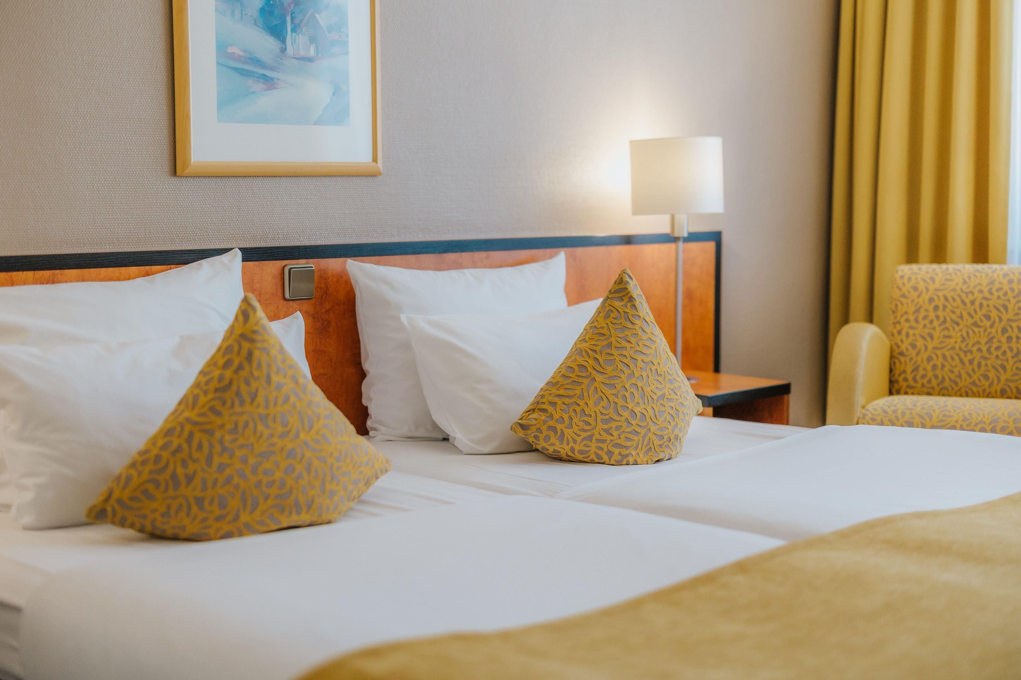 Habitación de hotel con una cama, dos almohadas, una mesita de noche, una lámpara y una silla.