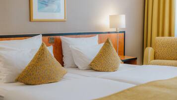 Habitación de hotel con una cama, dos almohadas, una mesita de noche, una lámpara y una silla.