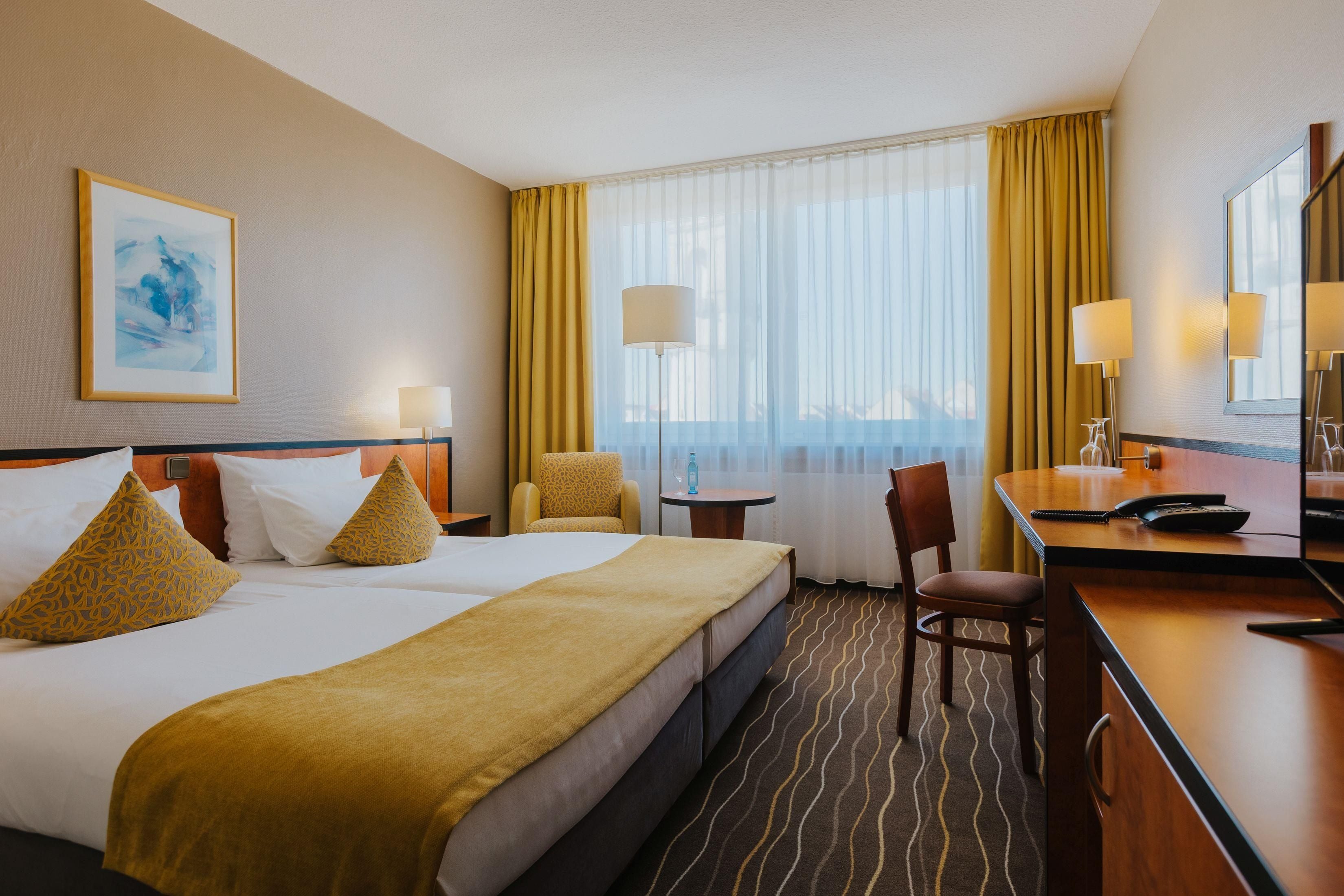 Habitación de hotel con una cama grande, dos sillas, un escritorio y una ventana con cortinas.