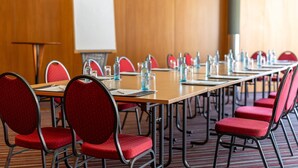 Una sala de conferencias con una larga mesa, sillas rojas, botellas de agua y una pizarra.