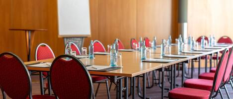 Una sala de conferencias con una larga mesa, sillas rojas, botellas de agua y una pizarra.