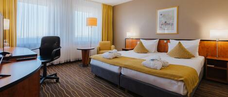 Habitación de hotel con cama, escritorio, silla, lámpara y un cuadro en la pared.