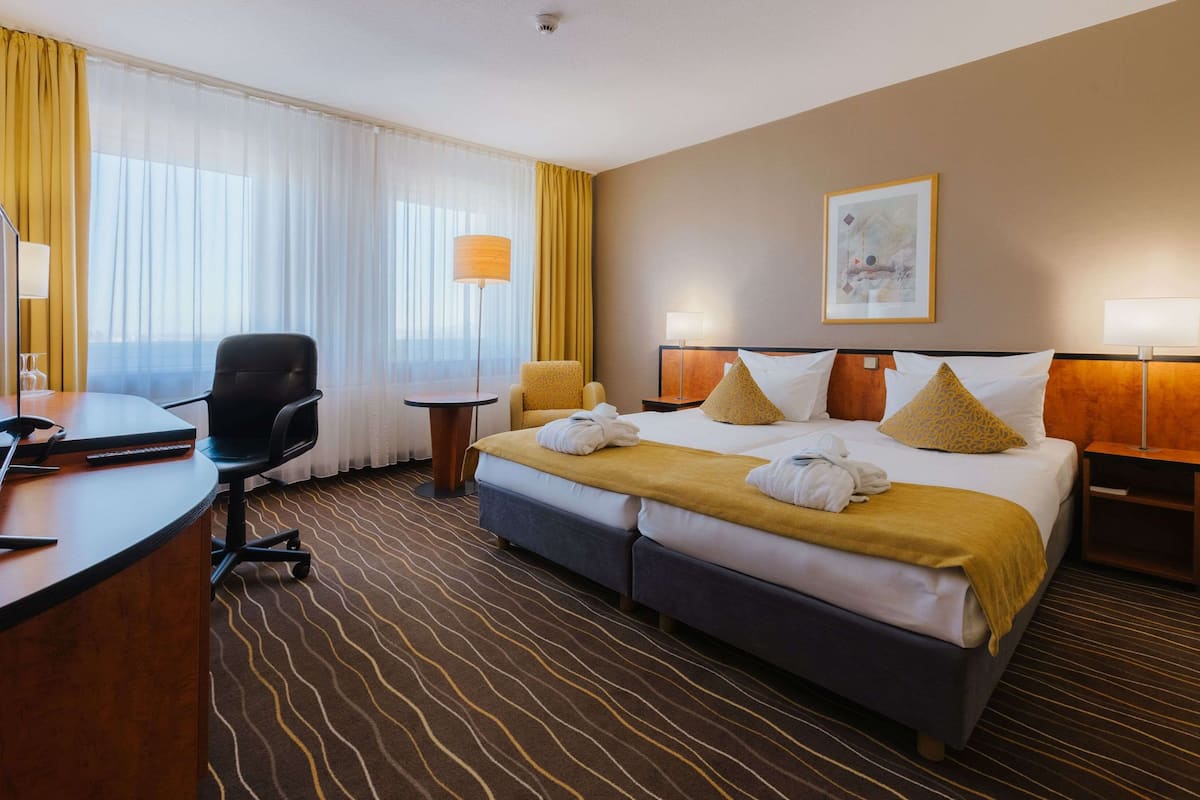 Quarto de hotel com uma cama, duas cadeiras, uma mesa e um abajur.