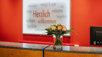 A reception desk with a welcome sign in multiple languages and a vase of flowers.