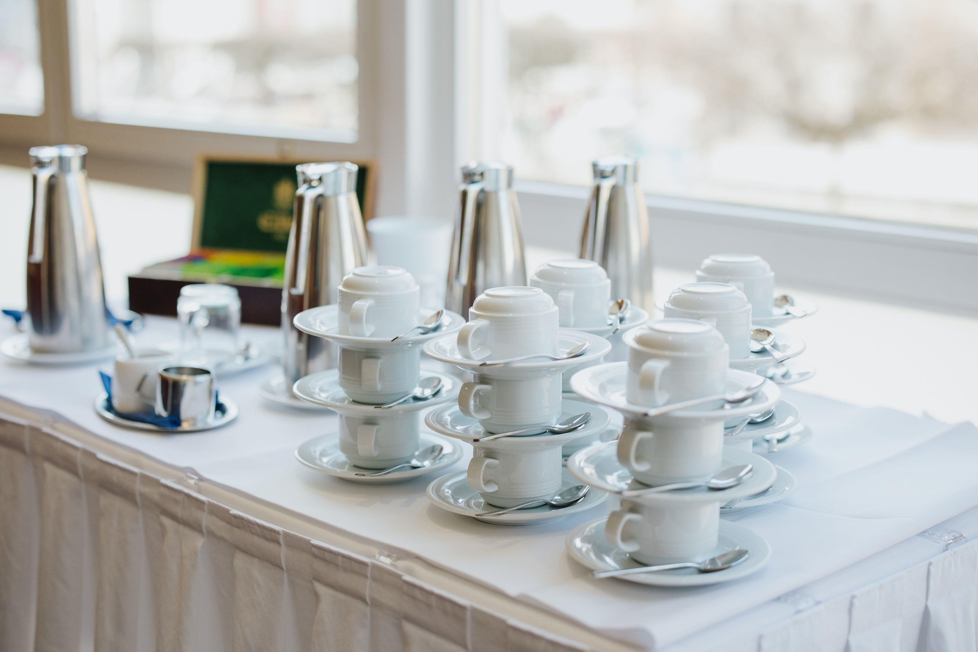 A table with multiple white teapots and cups arranged neatly.