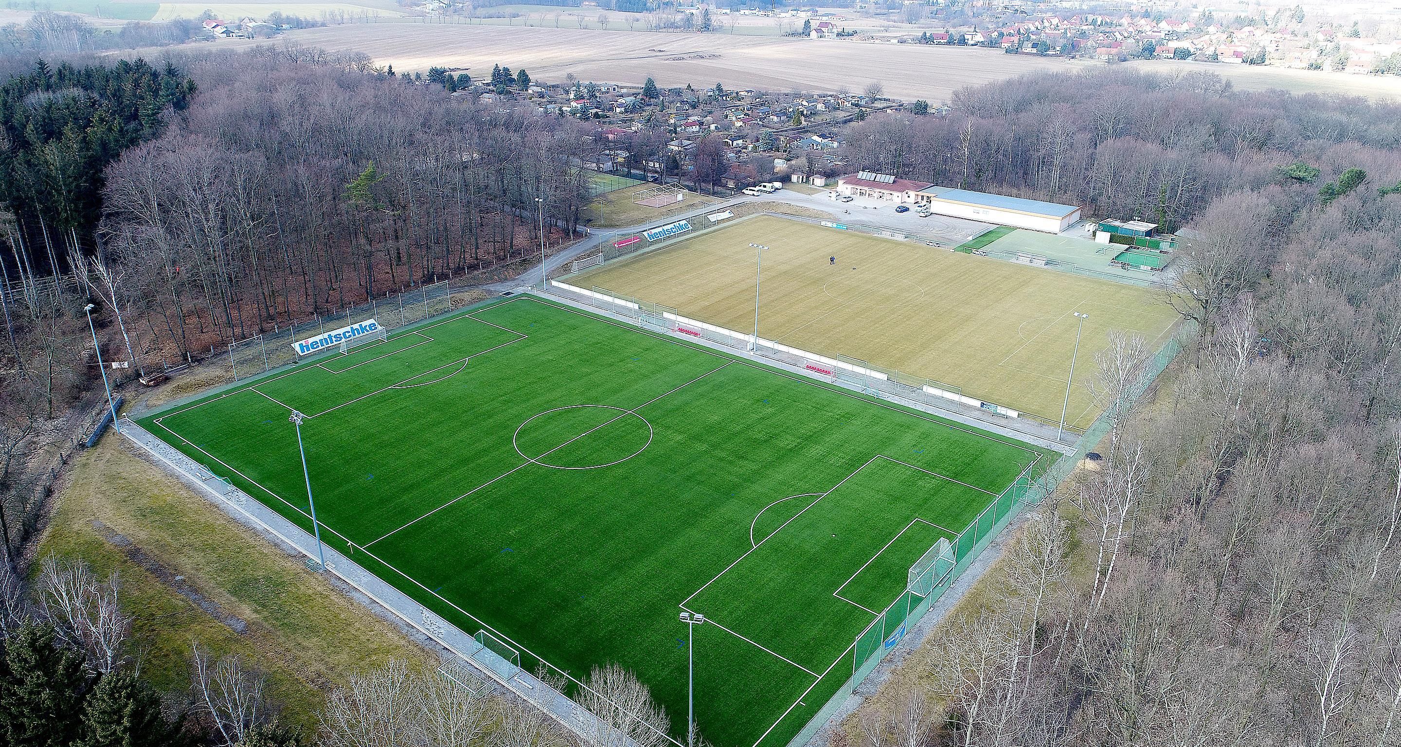 An aerial view of a sports field with a goalpost, surrounded by trees and buildings.