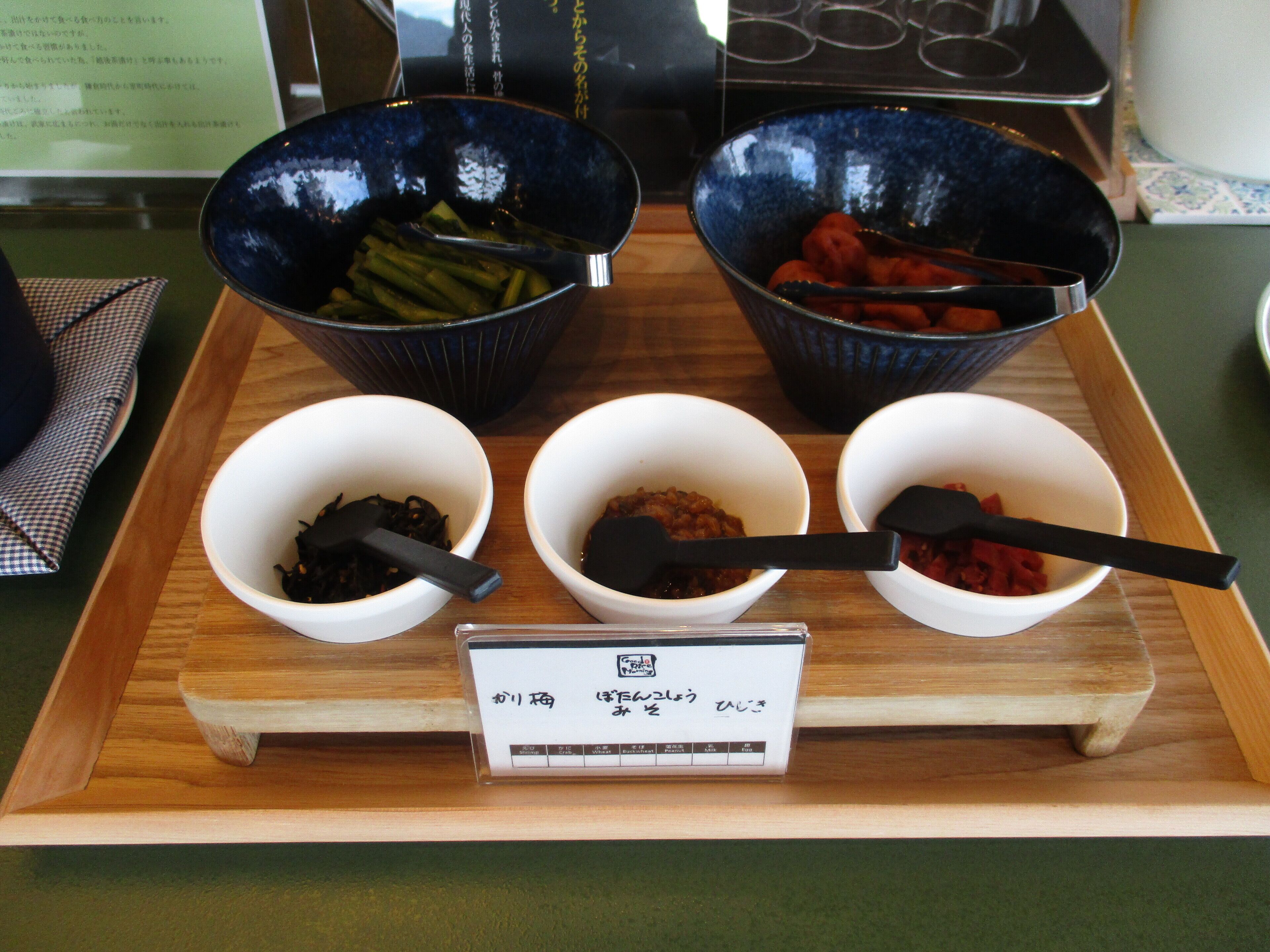 A wooden tray with four bowls containing different food items, each with a black spoon.