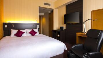 A hotel room with a large bed, a TV mounted on the wall, a massage chair, and a desk with a lamp.