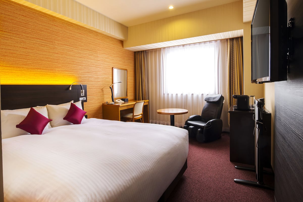 A hotel room with a large bed, a desk with a chair, a small round table, a TV, and a sofa.
