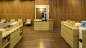 A hotel lobby with wooden paneling, a reception desk, seating area, and a coffee machine.