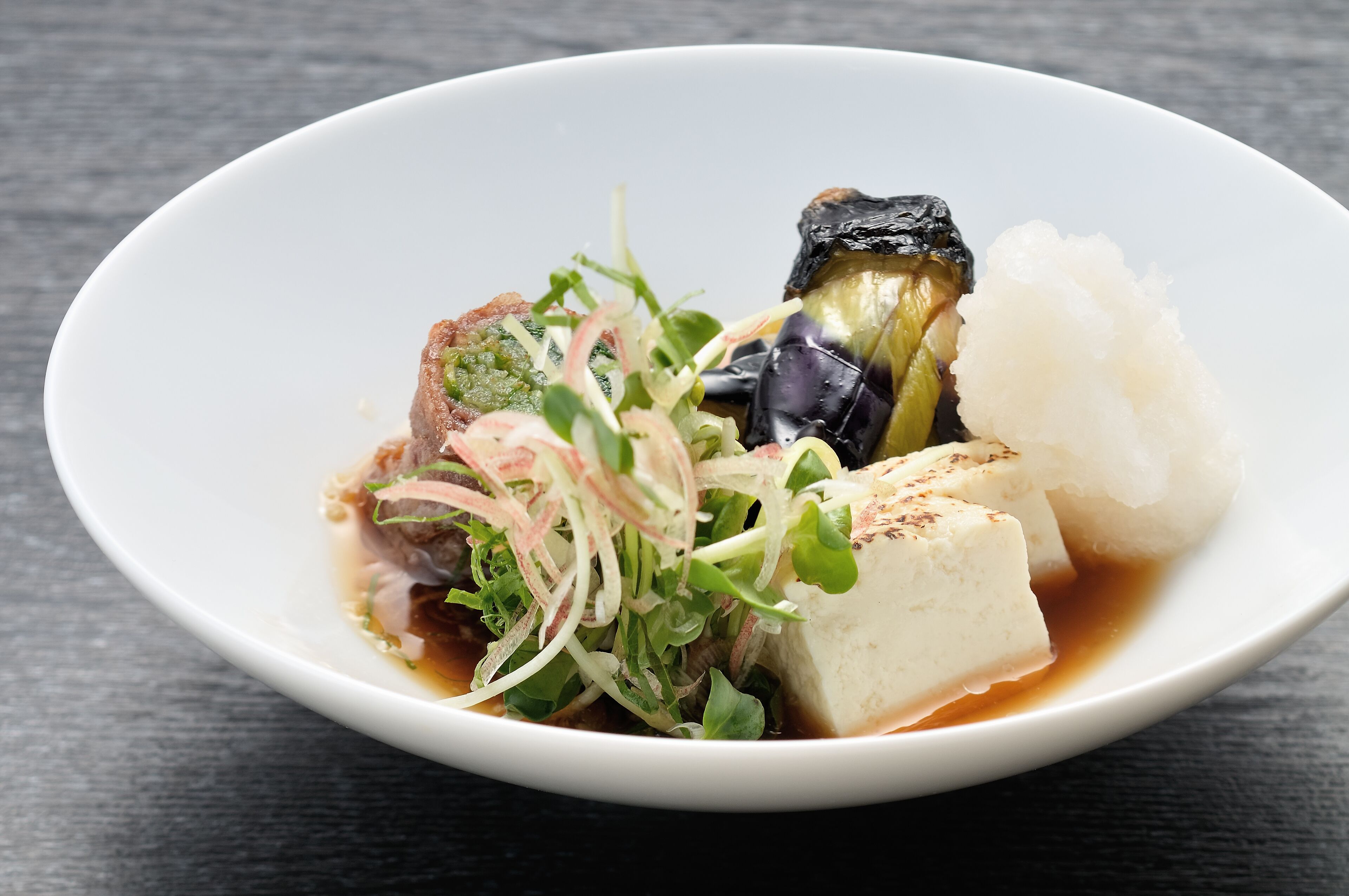 A white bowl containing a dish with tofu, vegetables, and a sauce.