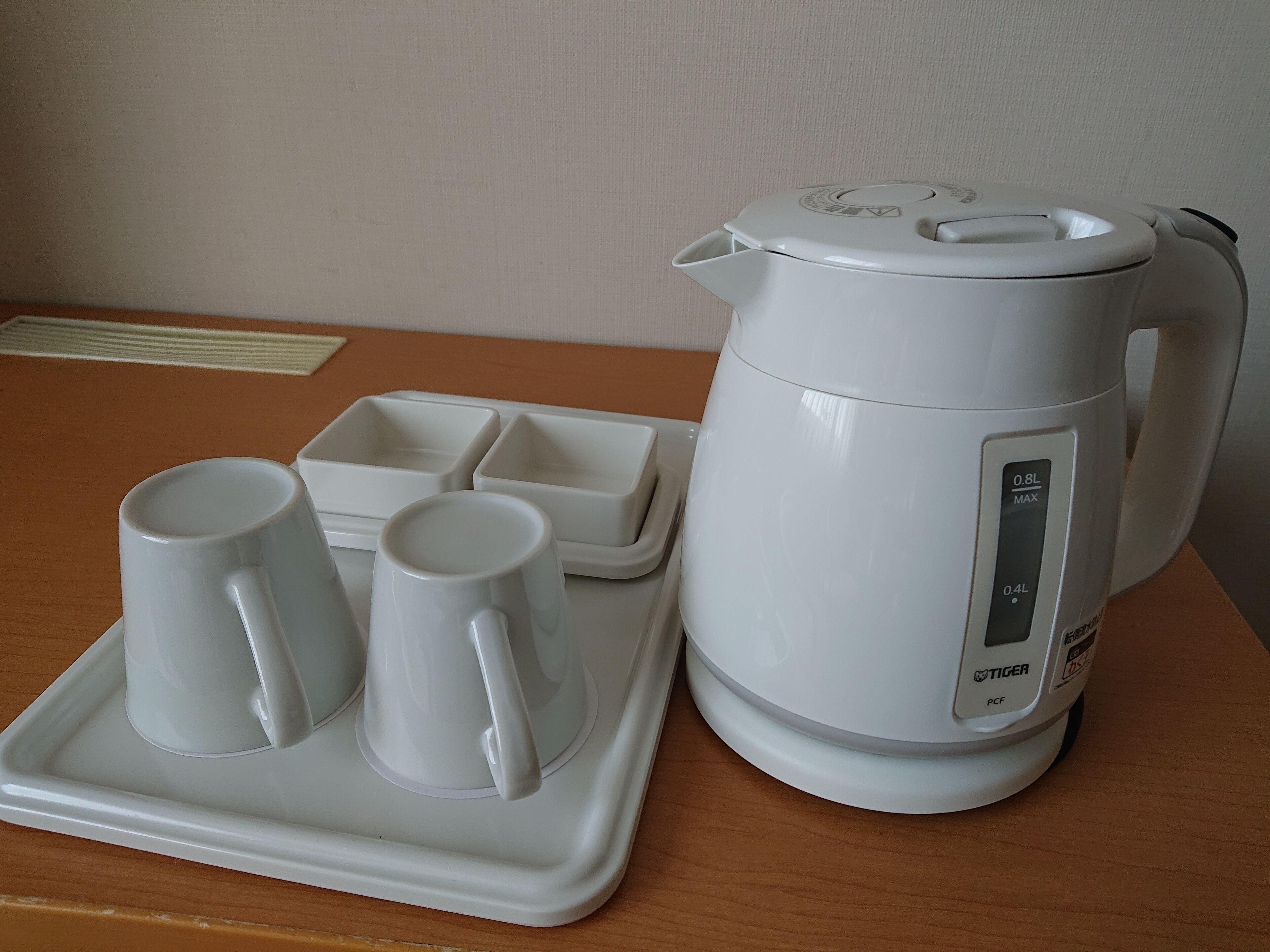 A white electric kettle with a digital display and a tray with two mugs on a wooden table.