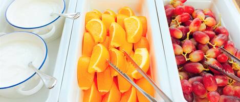 A buffet with three containers: one with orange slices, one with grapes, and one with a white creamy substance.