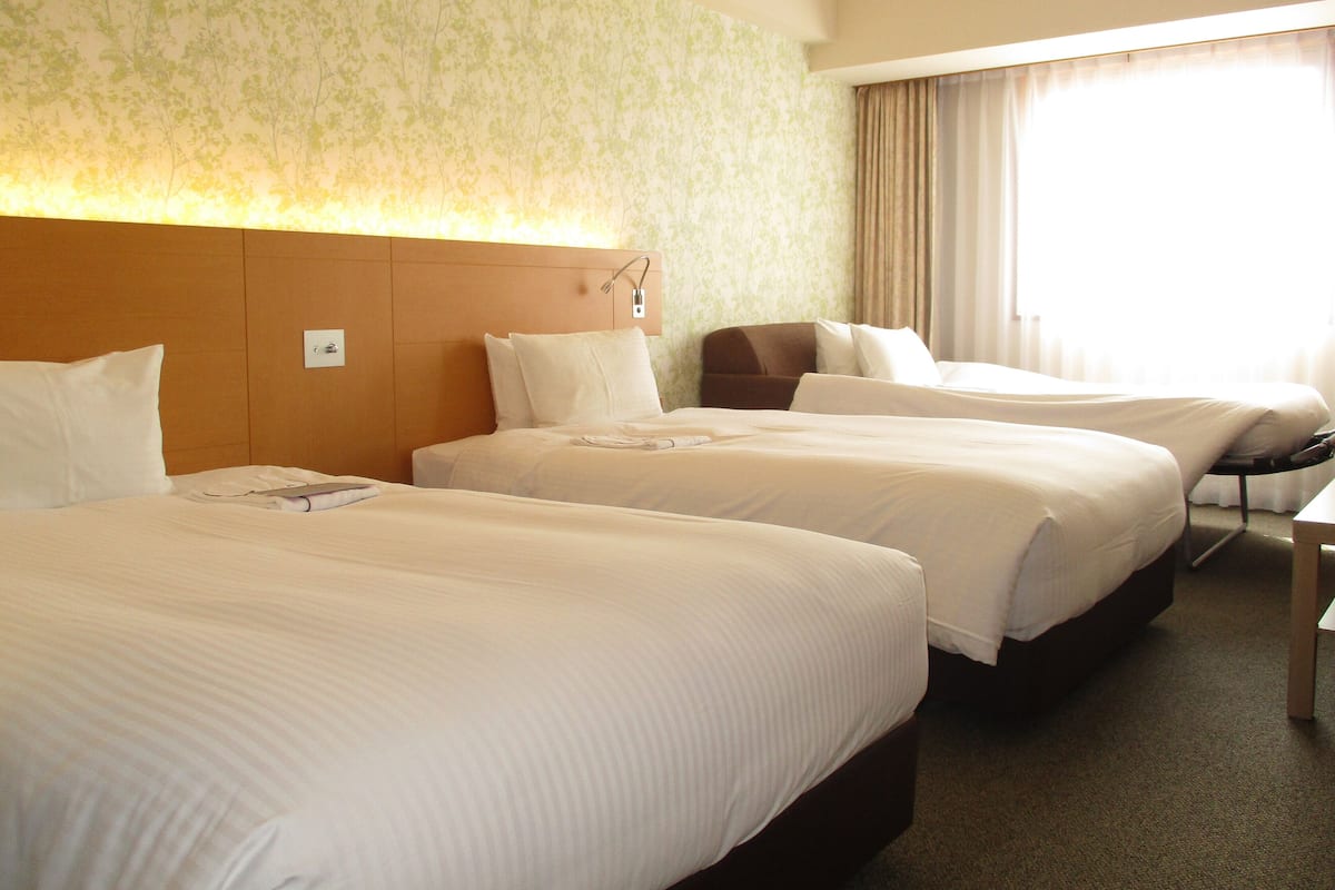 A hotel room with two beds, a headboard, a desk, and a window with curtains.