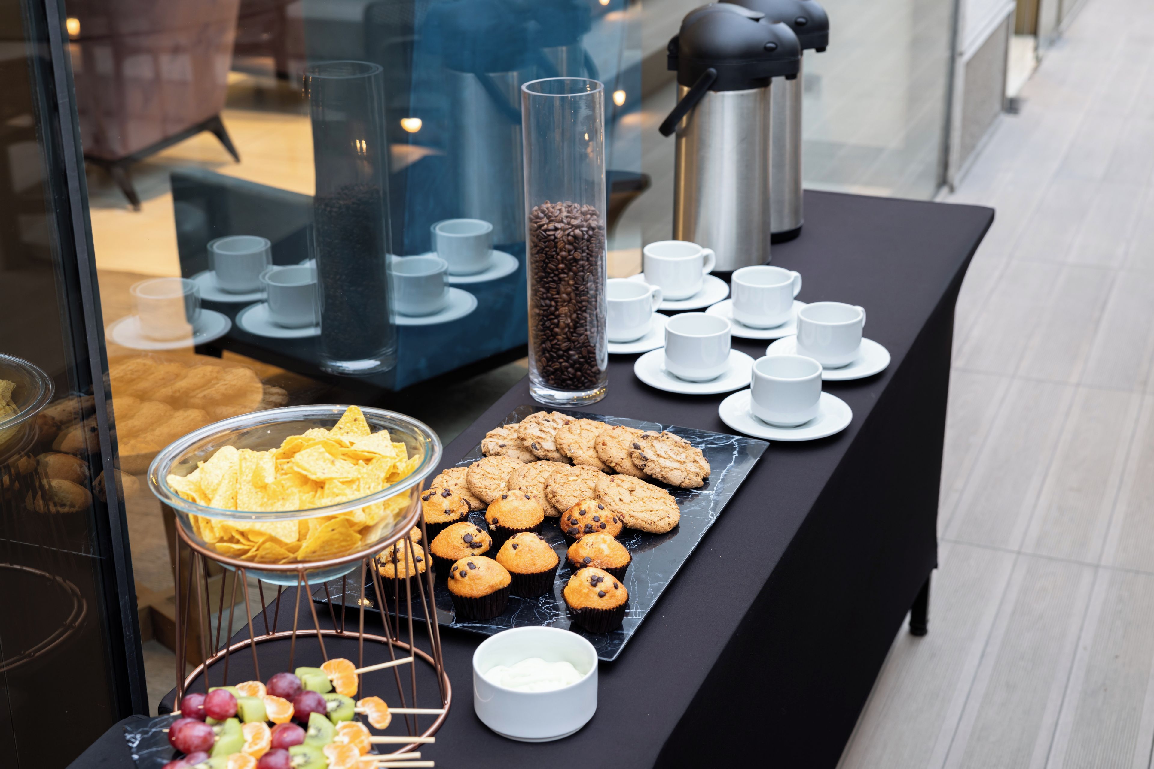 A buffet table with various food items, including cookies, chips, and fruit skewers.
