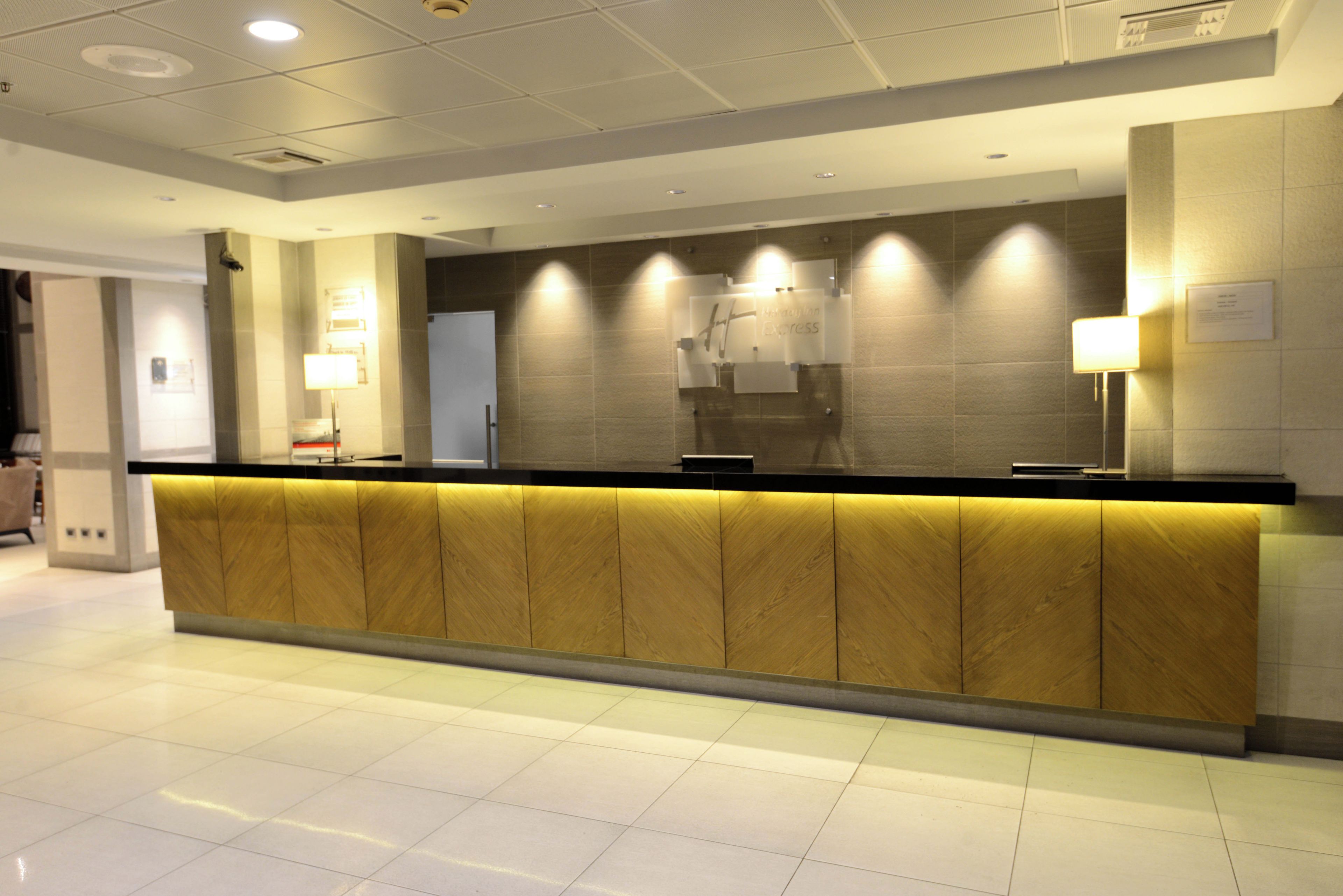 A reception desk with a wooden panel design, overhead lighting, and a tiled floor.